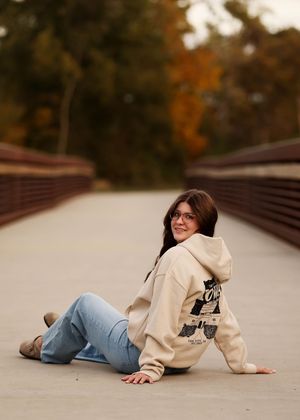 A casual portrait on a wooden bridge wearing a cream hoodie and jeans during autumn.