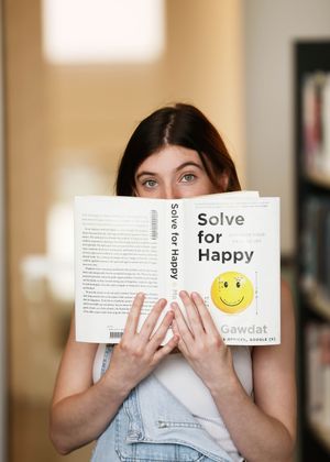 Reader holding up a self-help book titled 'Solve for Happy' with a smiley face.