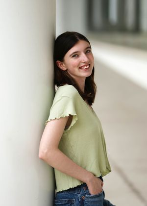Portrait of someone in a mint green top leaning against a white wall.