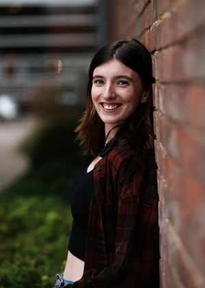 Portrait against a brick wall wearing a plaid flannel shirt.
