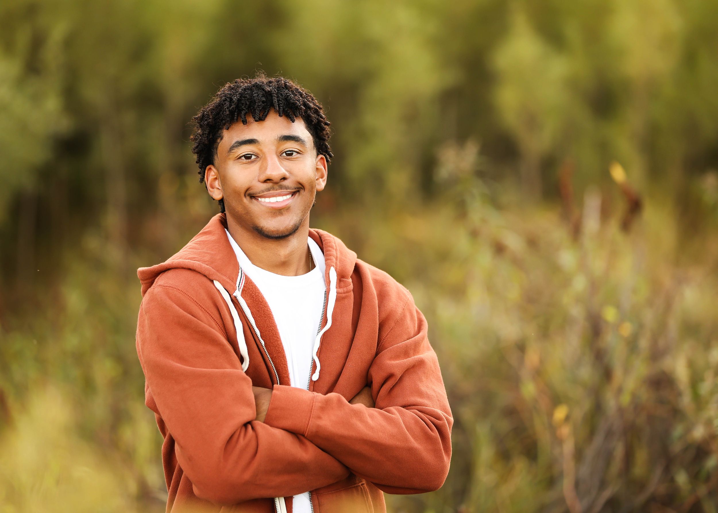 Person in orange hoodie smiling against natural outdoor background.
