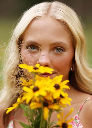 Blonde woman with blue eyes holding yellow black-eyed Susan flowers close to her face outdoors.