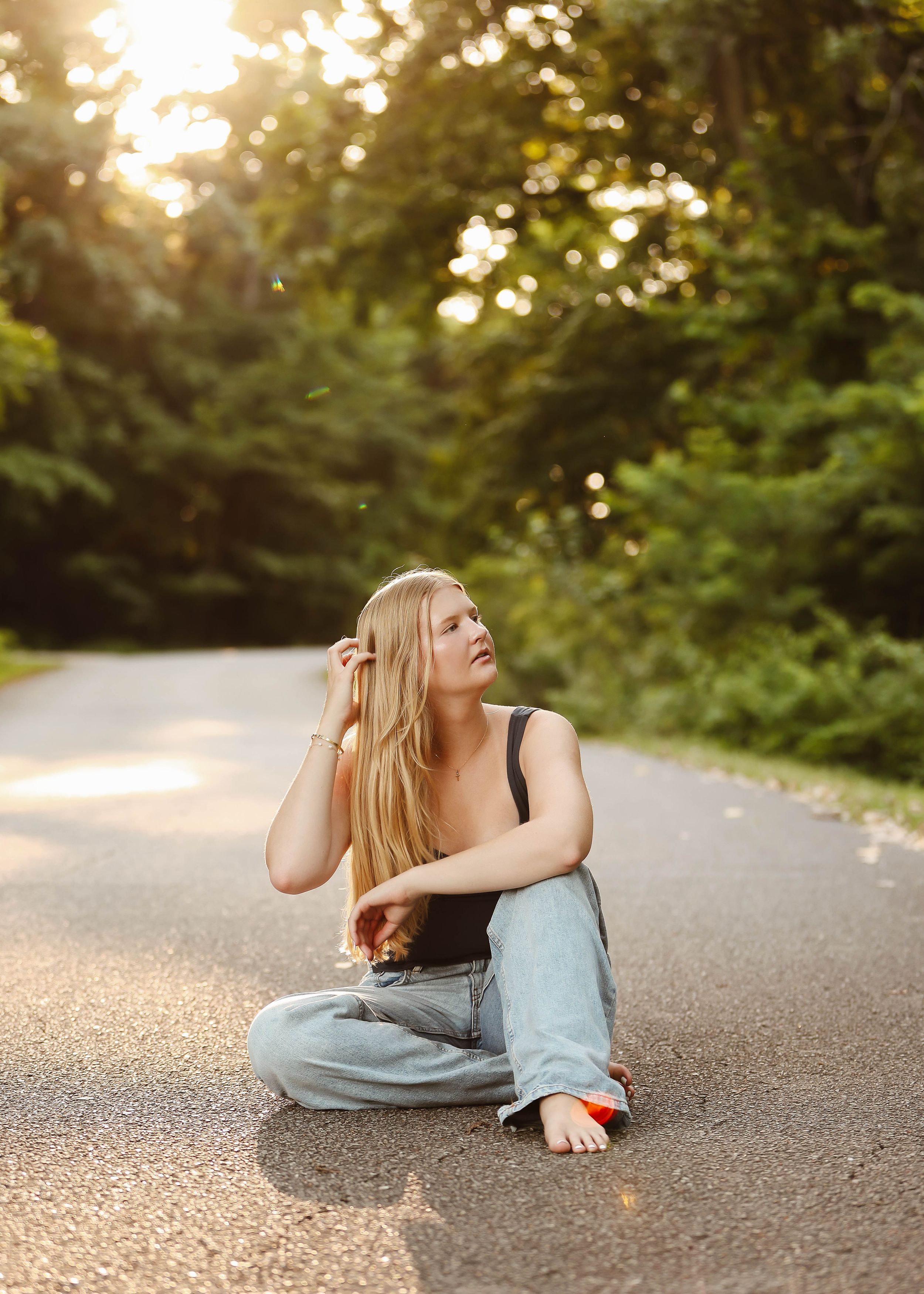 Figure lying on a gravel path surrounded by trees in warm evening light.