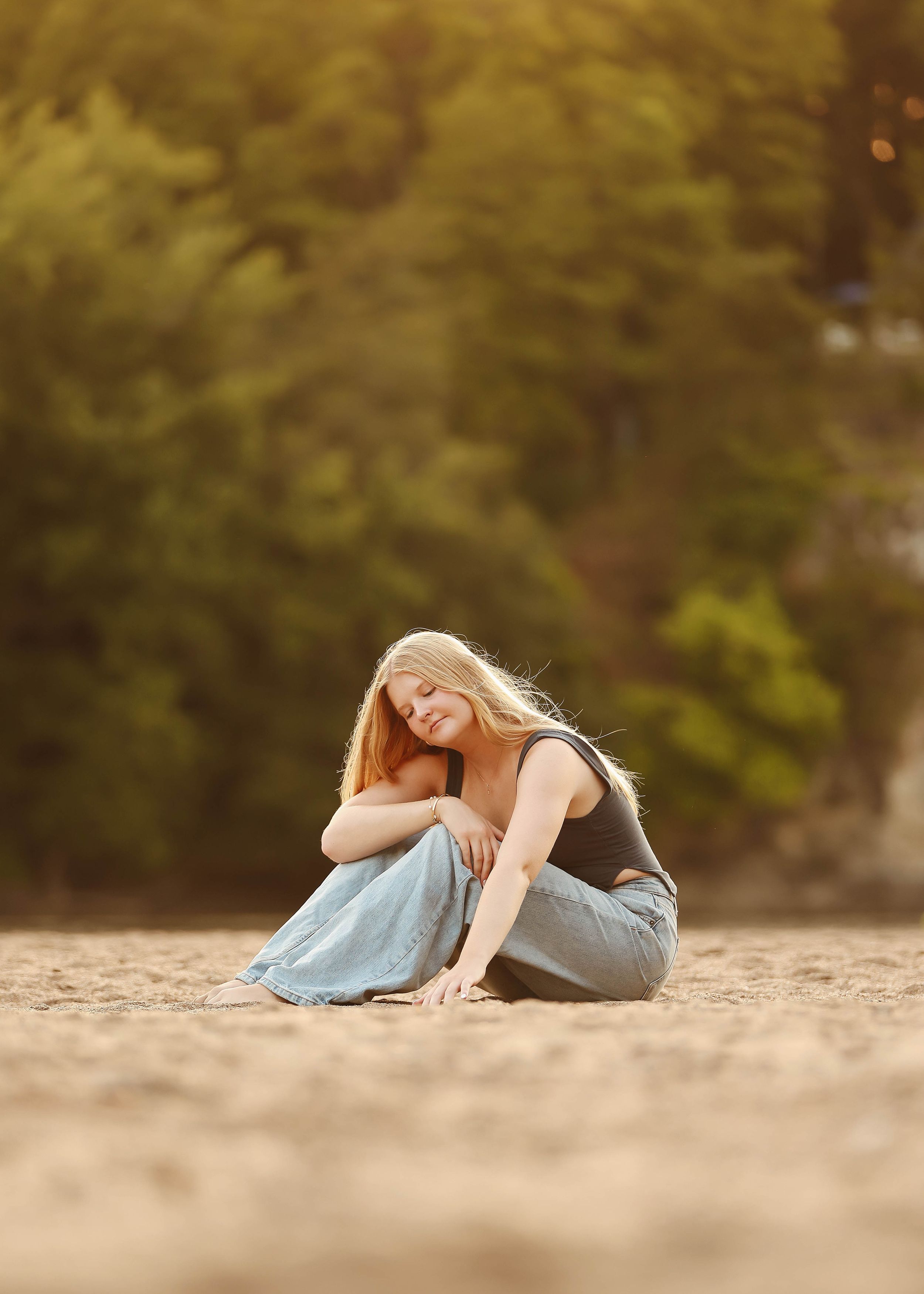 Person in casual attire posing on ground during golden hour photography session.