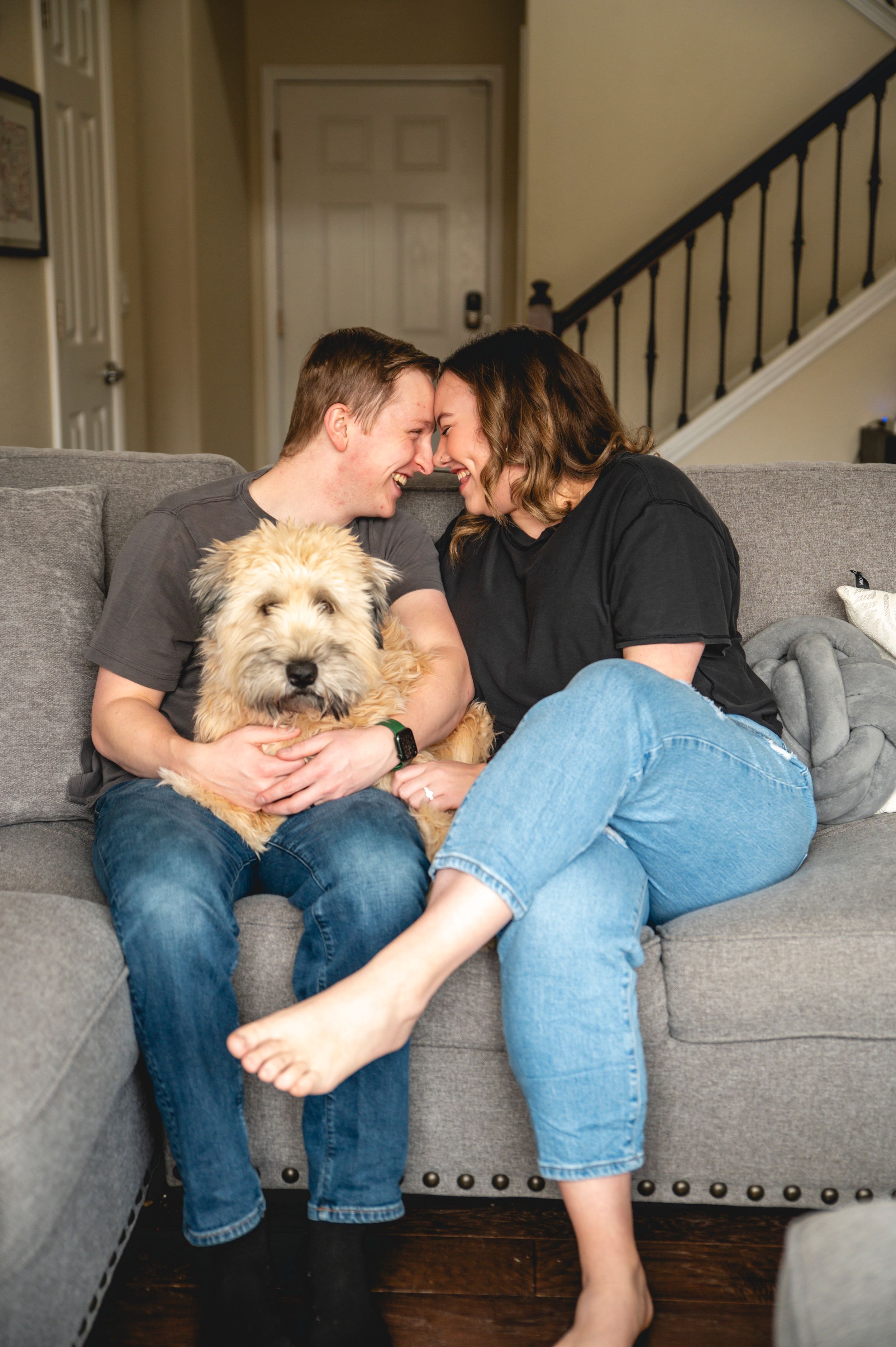 Couple relaxing on grey couch with fluffy white dog in casual home setting.
