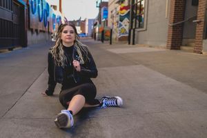 Someone sitting on sidewalk wearing casual clothes with colorful graffiti wall in background.