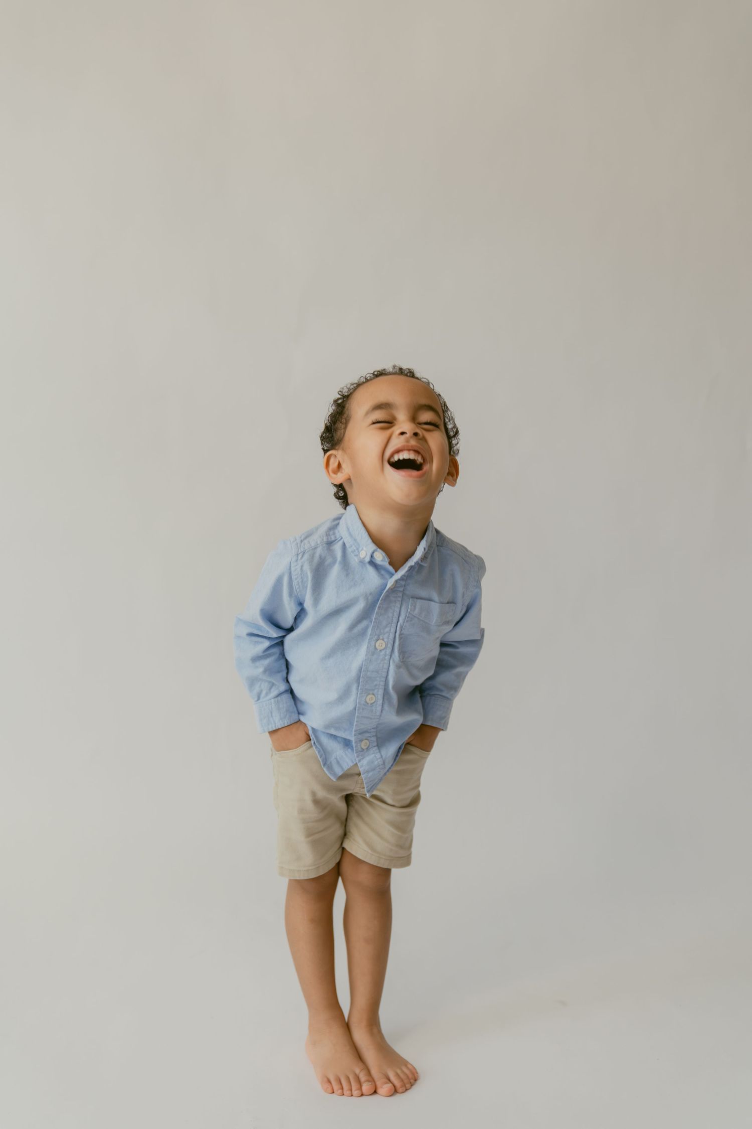 A sequence of four photos showing a child in a blue shirt and khaki shorts laughing with increasing joy against a gray backdrop.