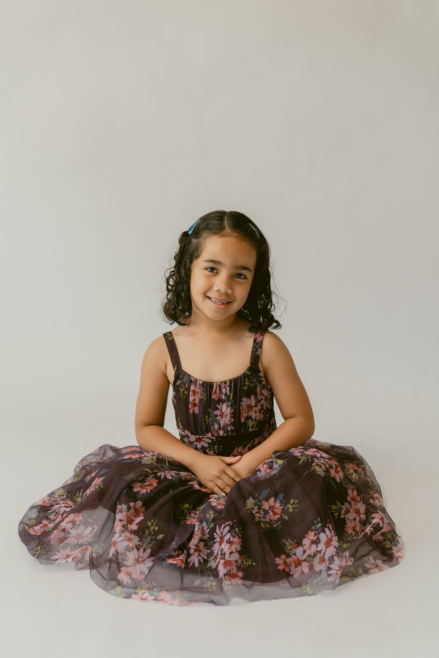 A child in a floral print dress with tulle overlay poses gracefully in three similar studio portraits against a light background.
