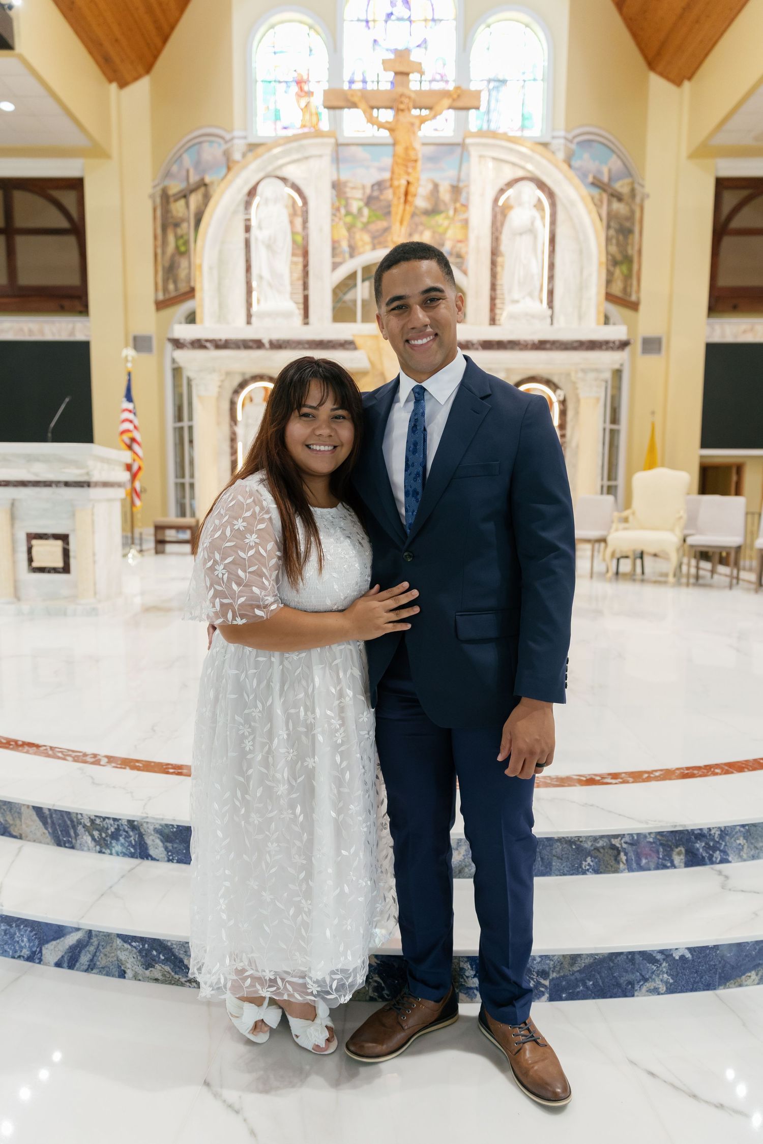A couple poses together inside a church with wooden ceiling beams and religious artwork visible in the background.