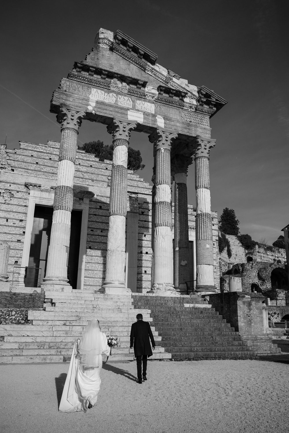 Ancient Roman temple ruins with Doric columns stand against a dramatic black and white sky as visitors explore the site.