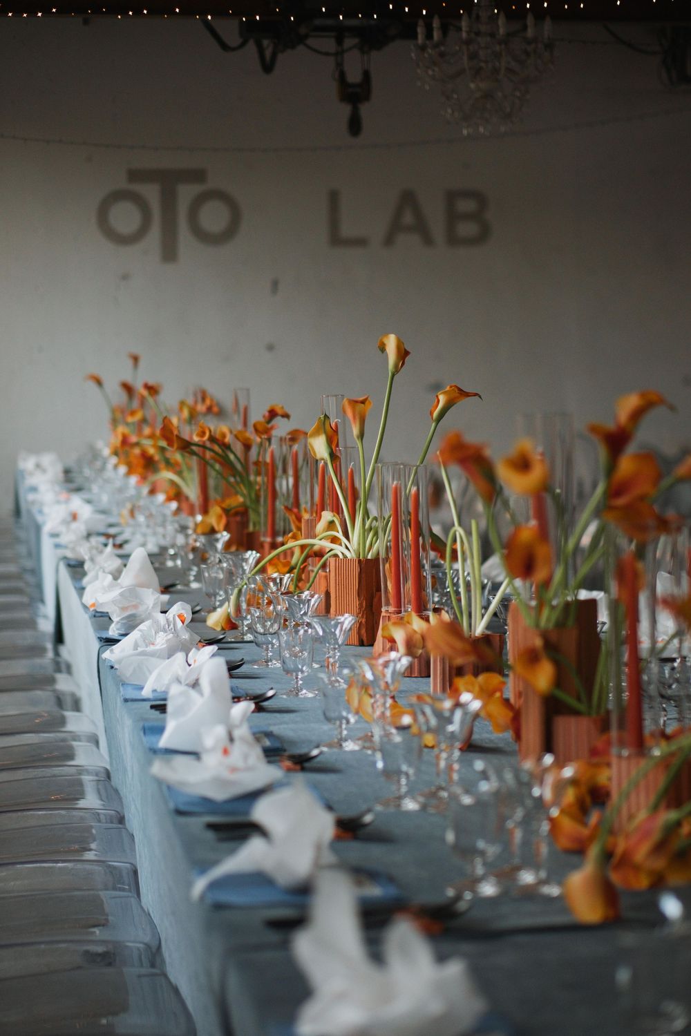 Elegant table setting with orange calla lilies and white linens at a modern reception venue.