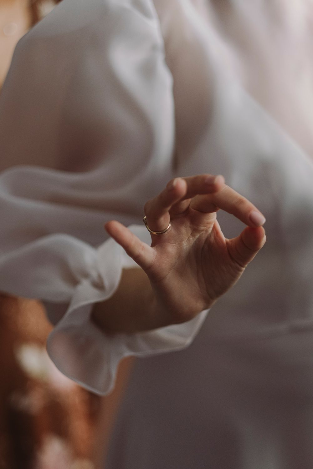 Close-up of hands delicately holding sheer white fabric in soft light.