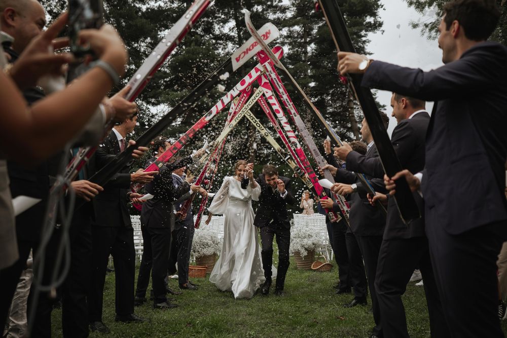 Wedding guests form an archway with pink ribbons for the newlyweds to walk through during an outdoor celebration.