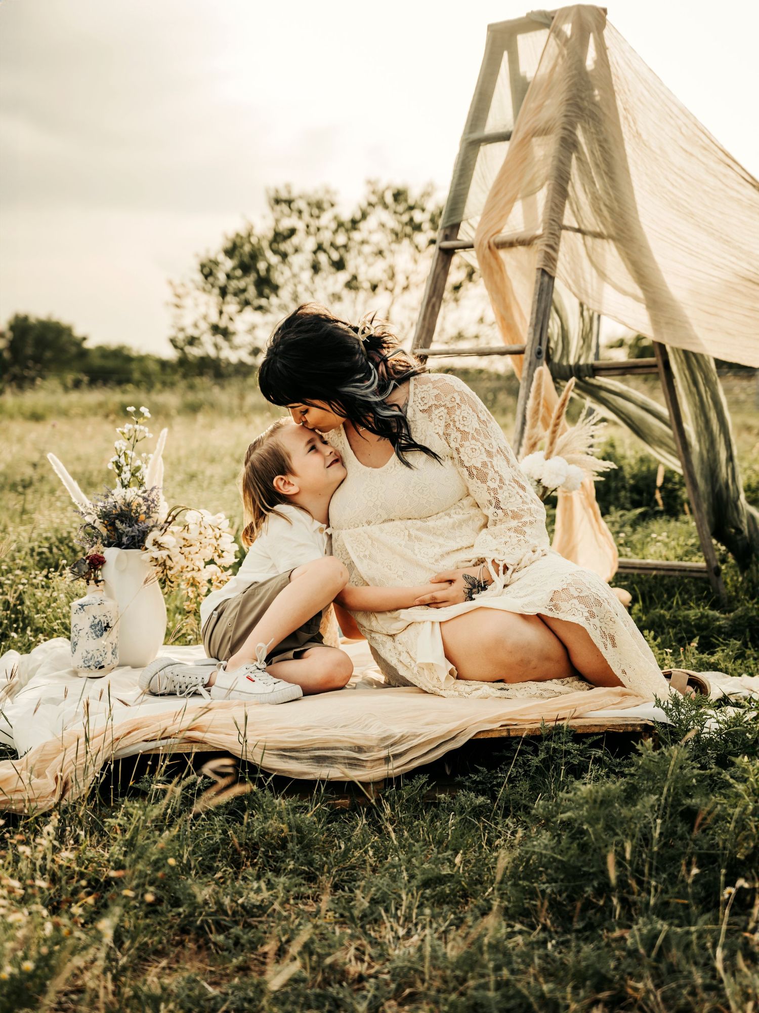 Mother and young son sitting on a blanket in a field, with a horse in the background, enjoying a peaceful moment together.