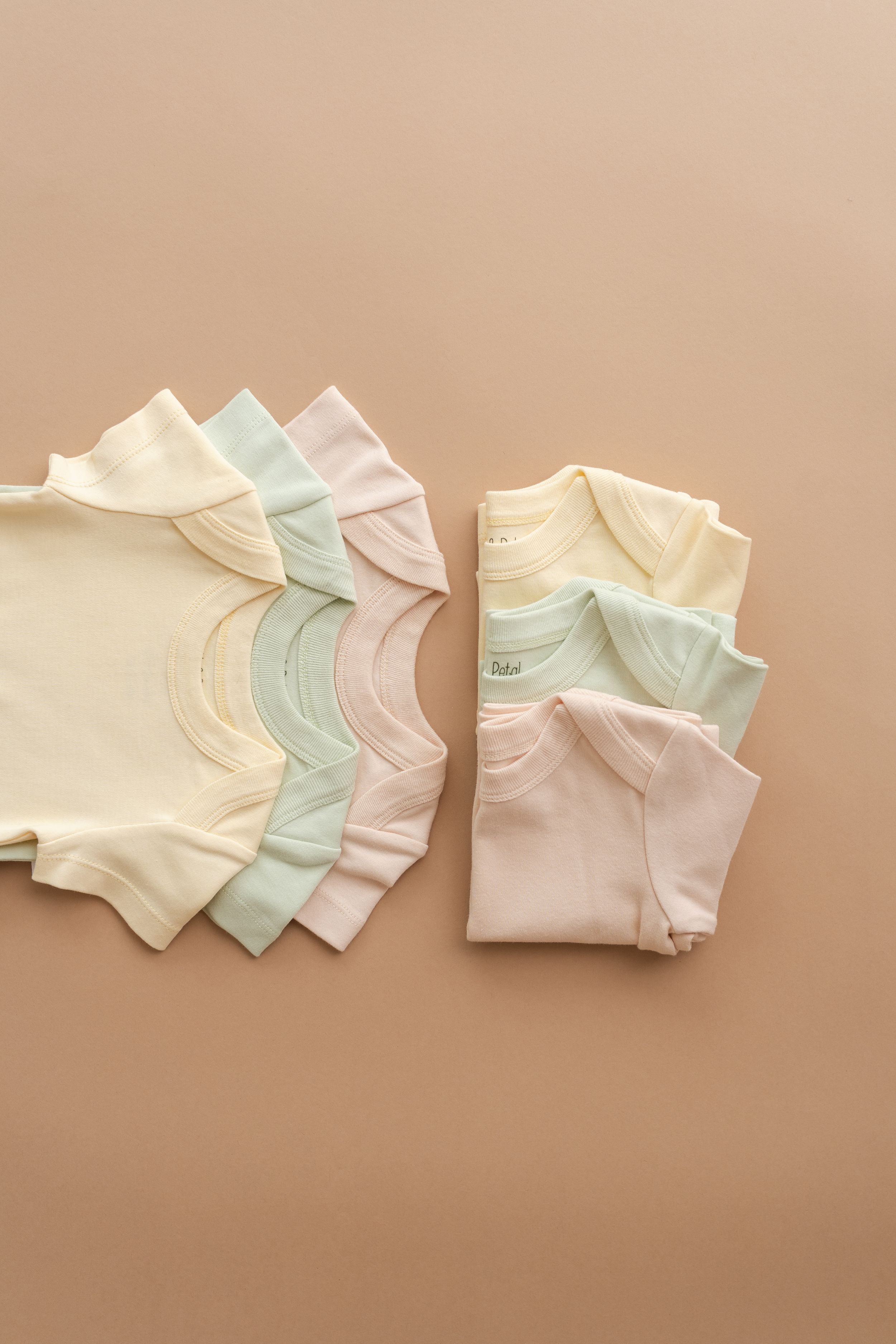 Collection of pastel colored baby onesies arranged neatly against beige background.