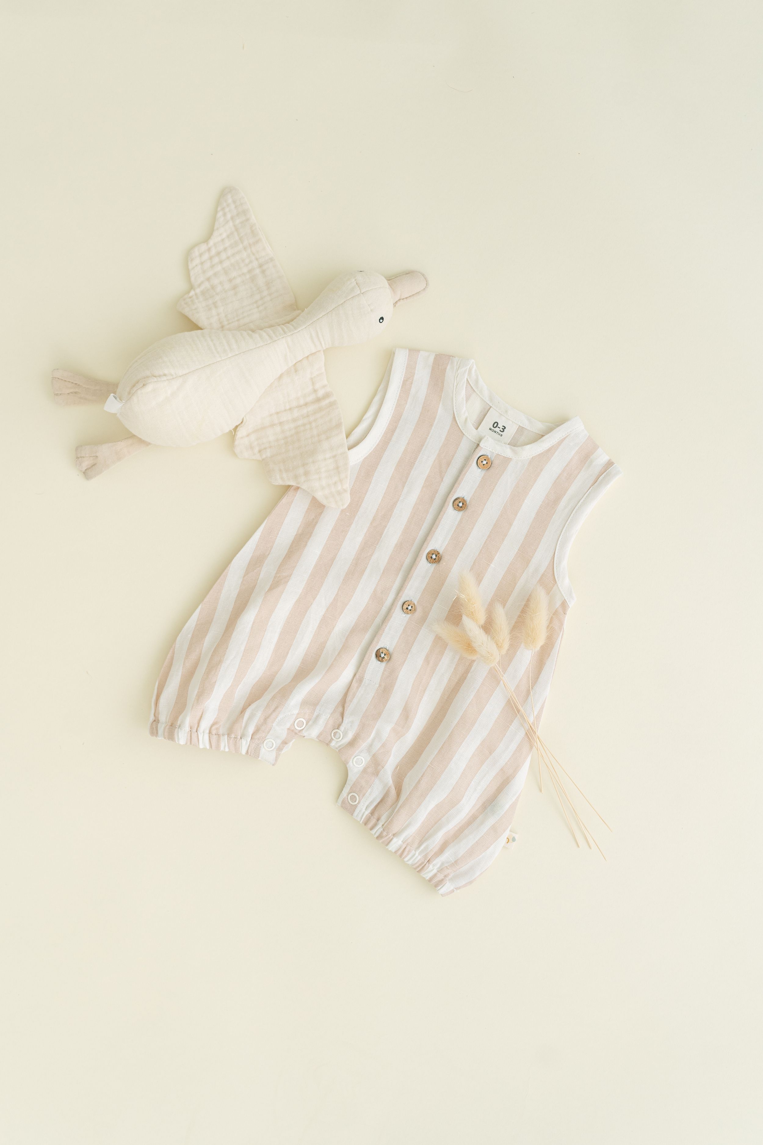 Striped baby romper and white plush toy bird on neutral background.