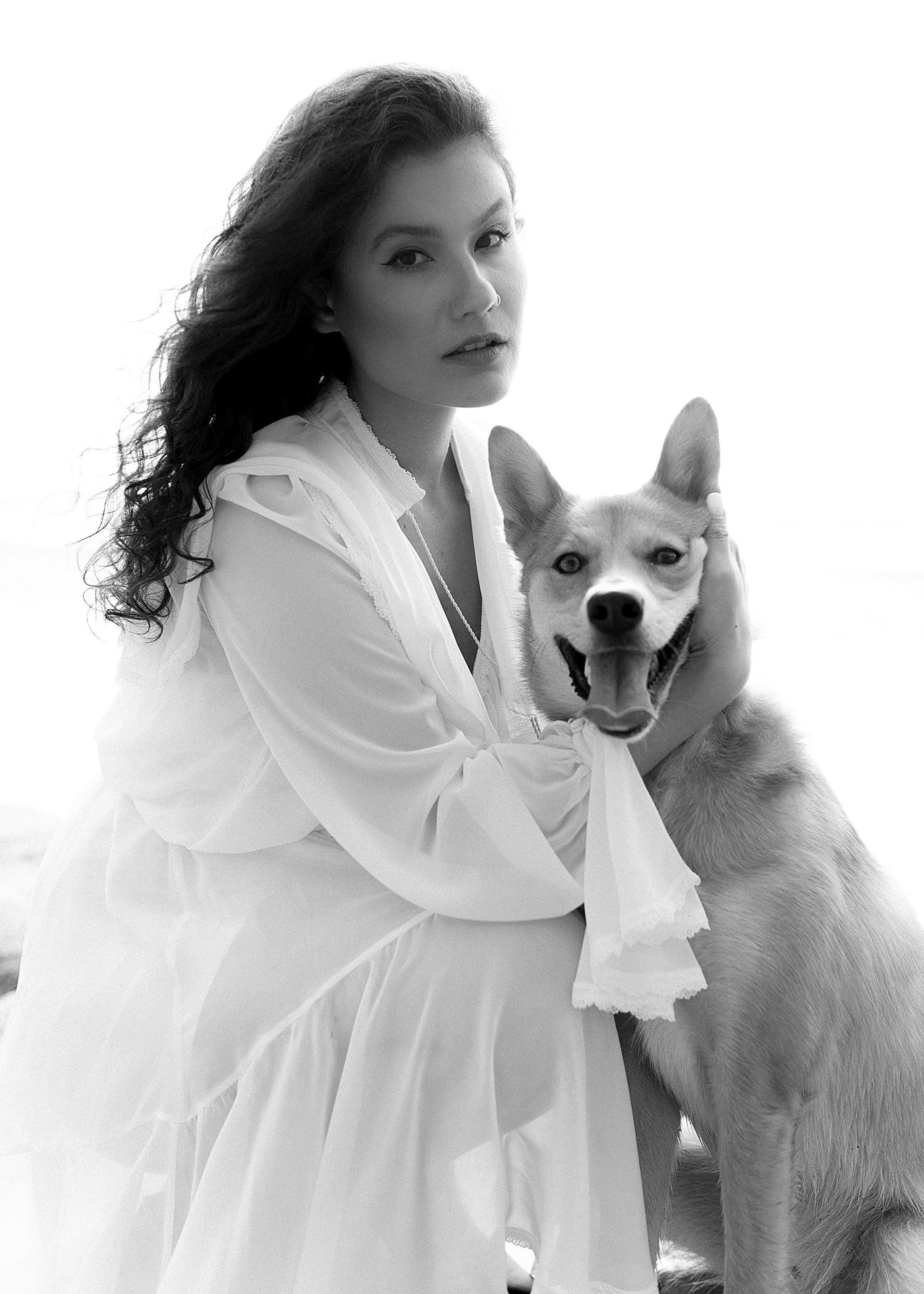 A white dog poses with someone wearing a white outfit against a bright background.