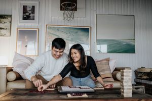 A couple playing Jenga in a cozy room decorated with surf artwork and a basketball hoop.