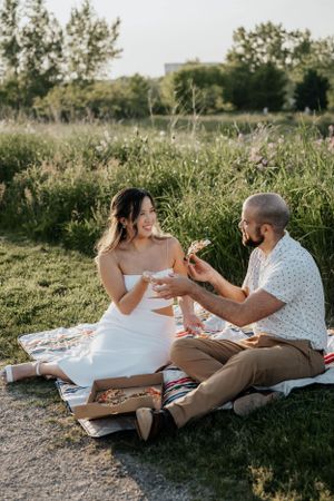 Casual outdoor picnic scene with couple sharing drinks on blanket in summer field.