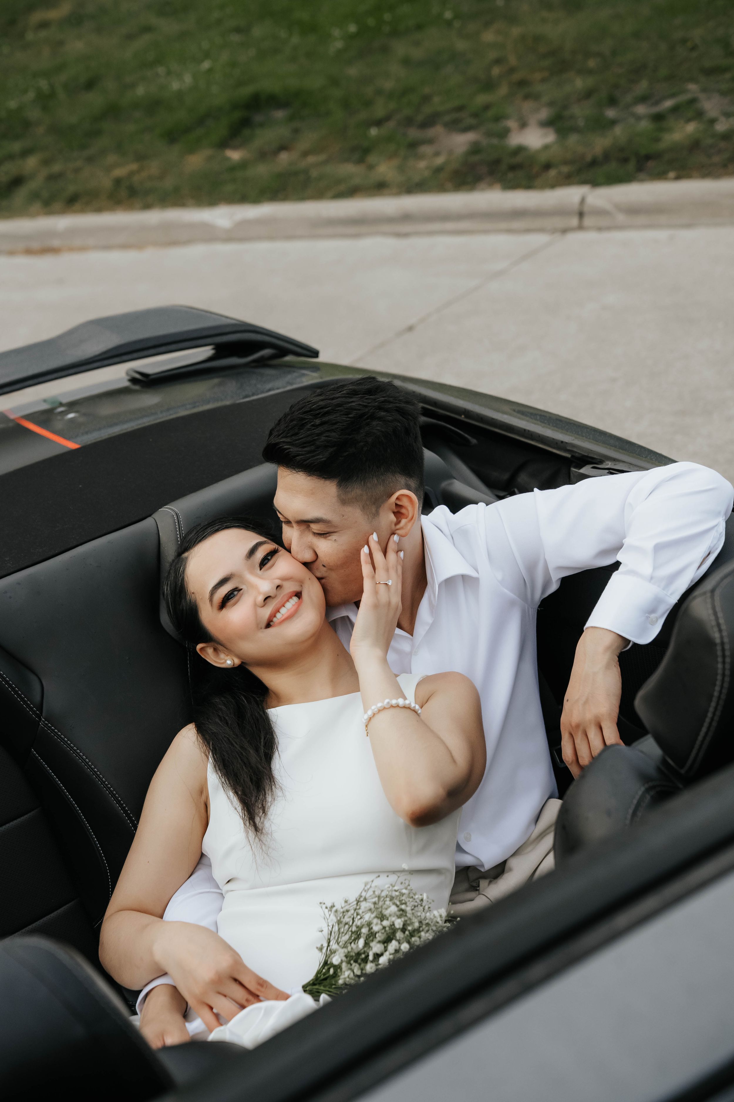 A couple shares an intimate moment while sitting in a black car with baby's breath flowers.