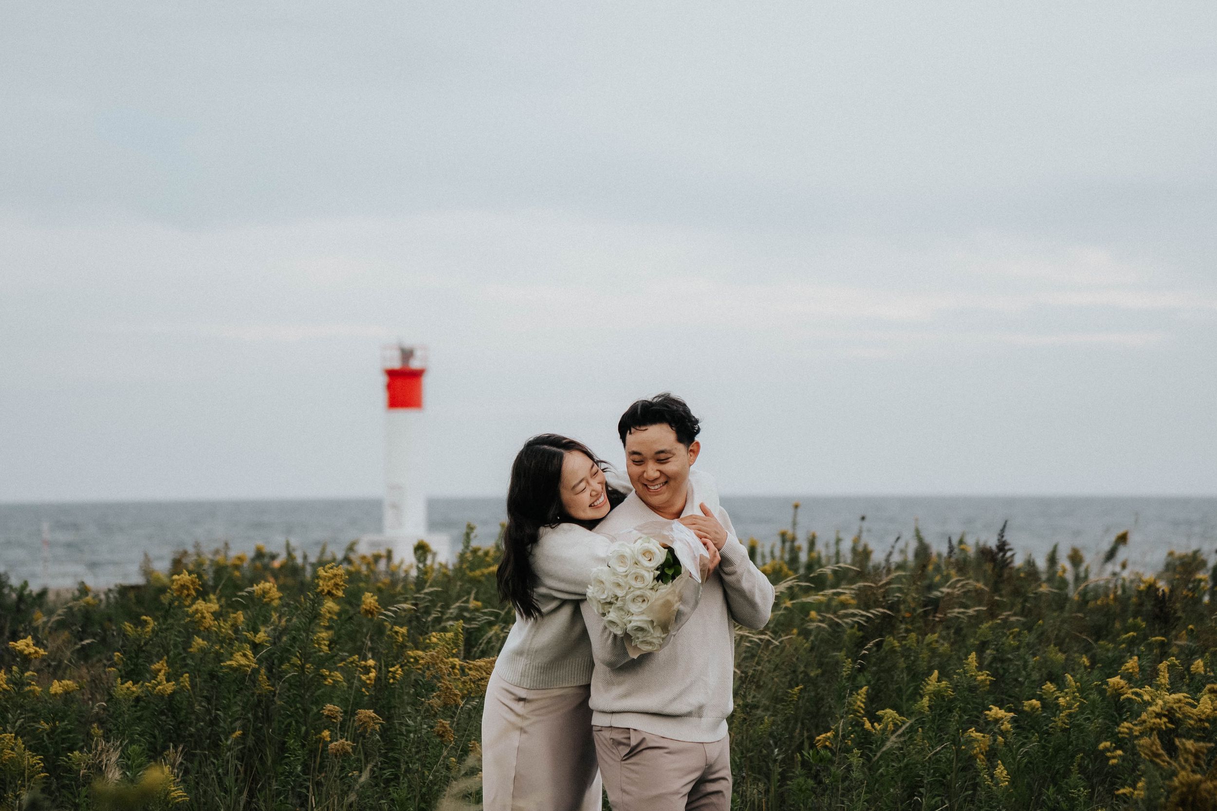 A couple shares a romantic moment together in a field of yellow wildflowers with the ocean in the background.