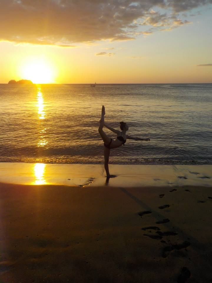 Girl doing a yoga pose on the beach with the sunset in the background.