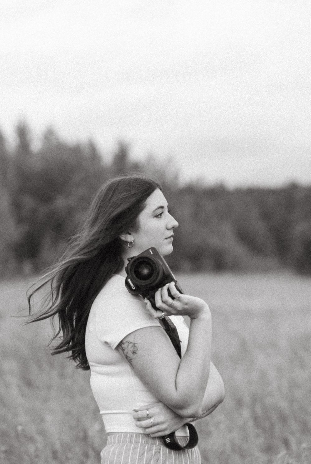 Photographer looking to the side holding her camera up by her face with hair blowing in the breeze.