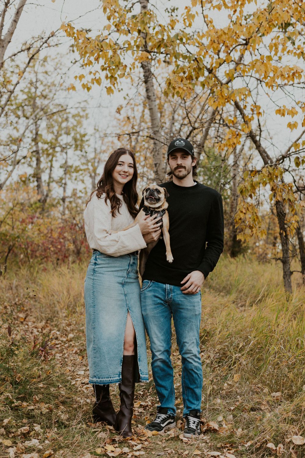 Man and woman standing holding their dog in the middle looking and smiling at the camera.