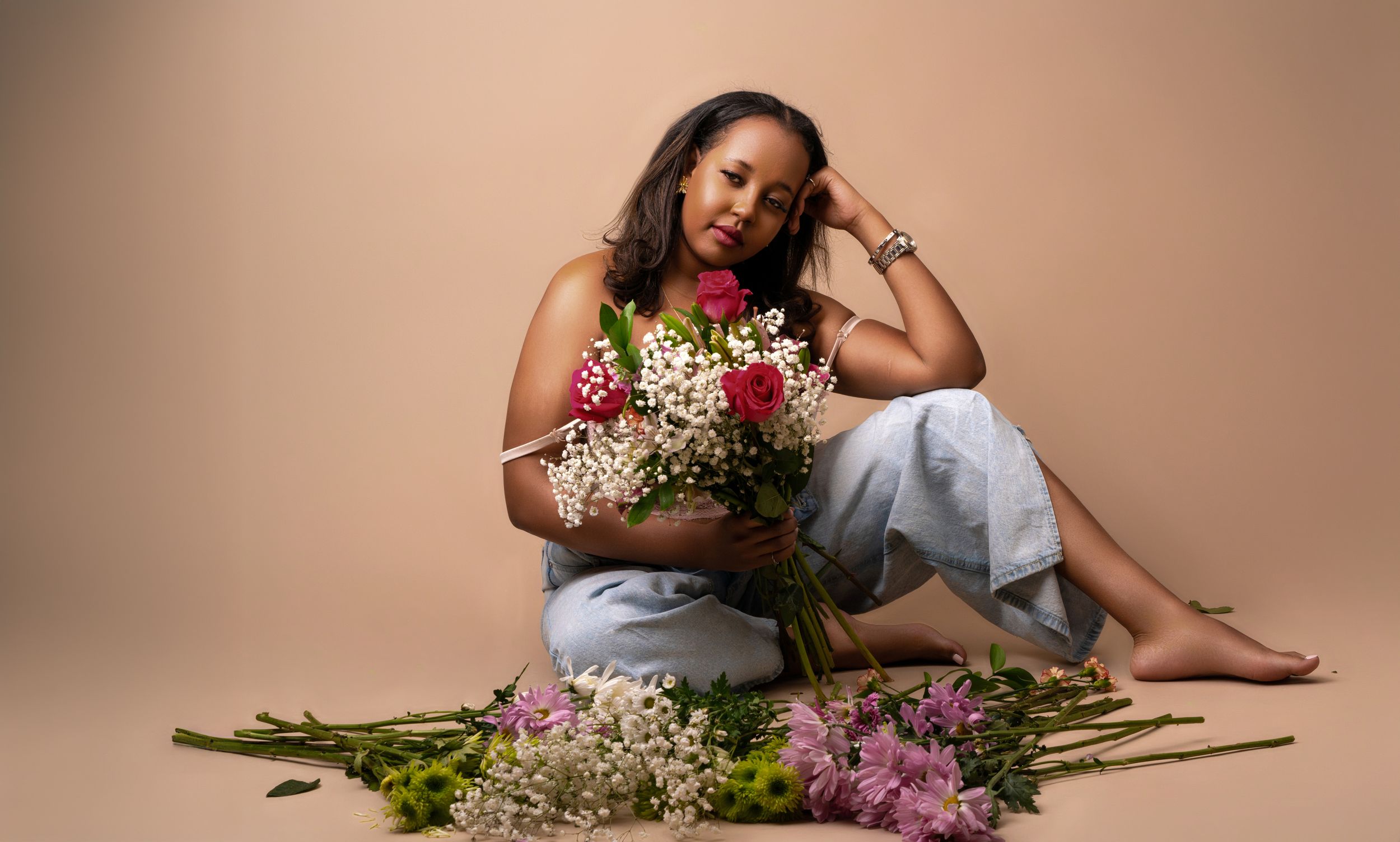 Casual portrait with mixed flower bouquet and denim against peachy backdrop.