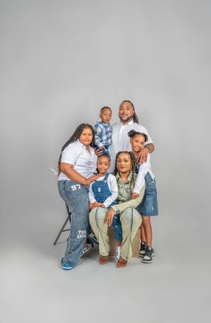 A family wearing white shirts and jeans poses together against a gray studio backdrop for a portrait session.