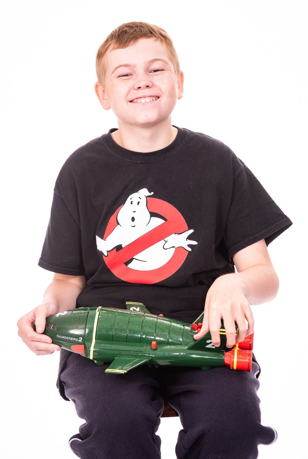 A person wearing a Ghostbusters t-shirt holds a vintage green toy airplane against a white background.