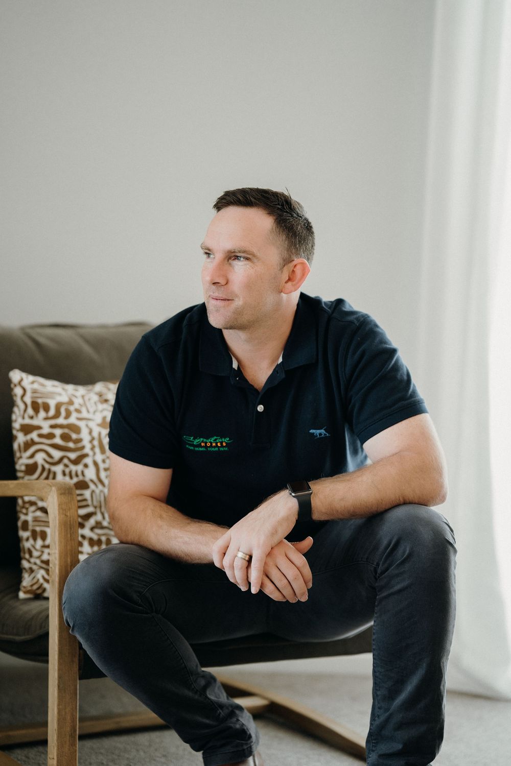 Person in a navy polo shirt sitting casually on a chair in a modern living room interior with decorative pillows.