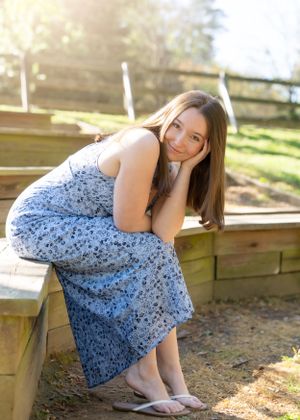 Senior portrait of young woman in floral dress posed on wooden steps outdoors.