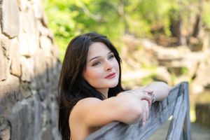 Portrait of a young woman leaning against stonework in outdoor setting with soft lighting.