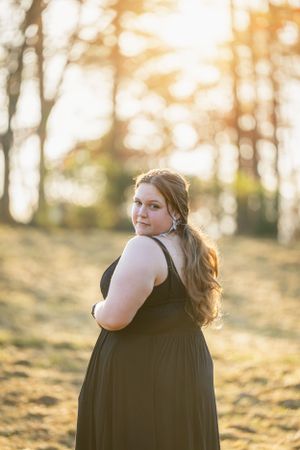 Portrait of woman in black dress at golden hour in outdoor setting.
