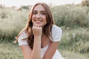 Portrait of someone in a white dress sitting in a sunlit meadow during golden hour.