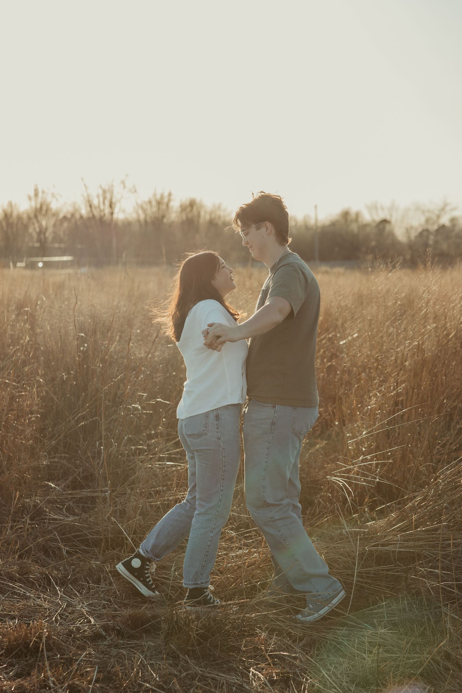 A couple dances playfully together in a golden sunlit field during sunset.