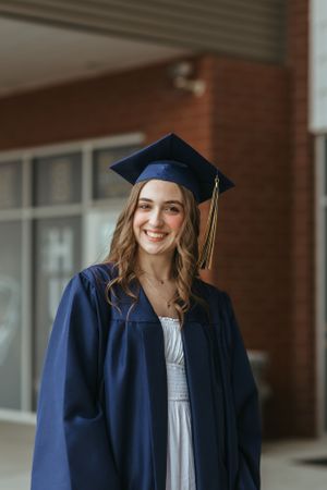 Graduate in navy blue cap and gown poses for portraits on brick campus building backdrop.