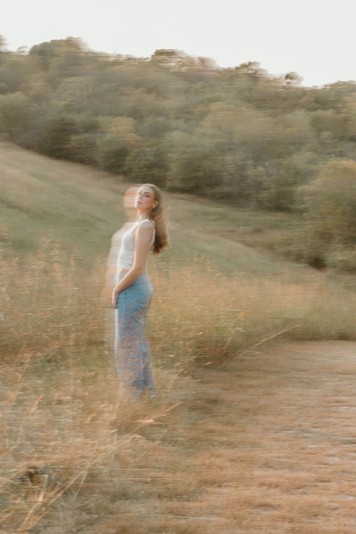 Dreamy portrait of senior in casual clothes standing in a field at dusk.