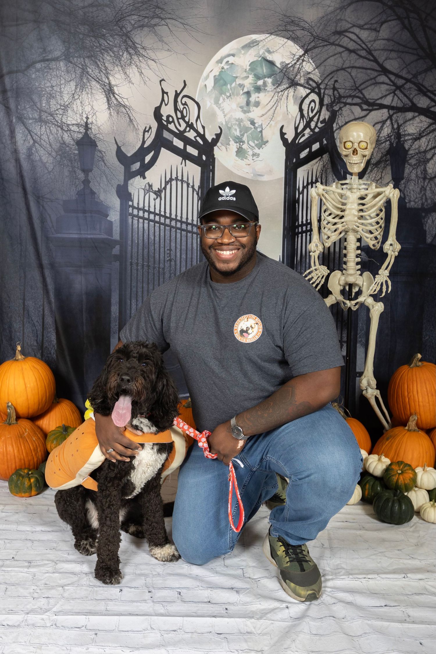 A cheerful person poses with their dog among Halloween decorations and pumpkins.