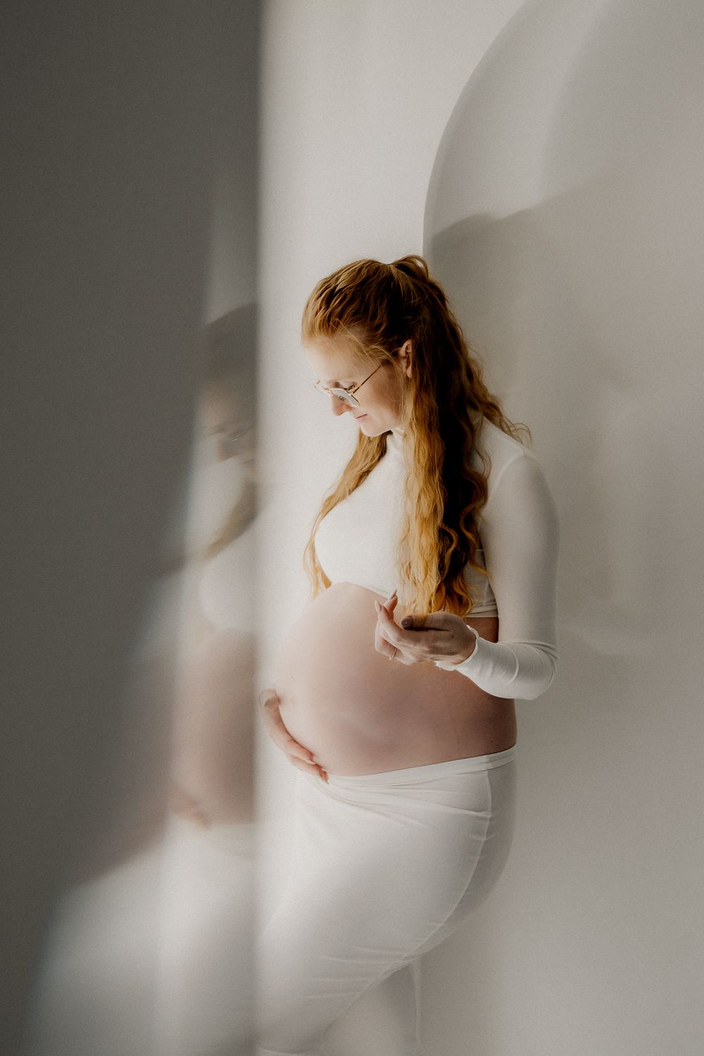 Artistic maternity photo series showing ethereal silhouettes of pregnant woman in white against soft neutral background.