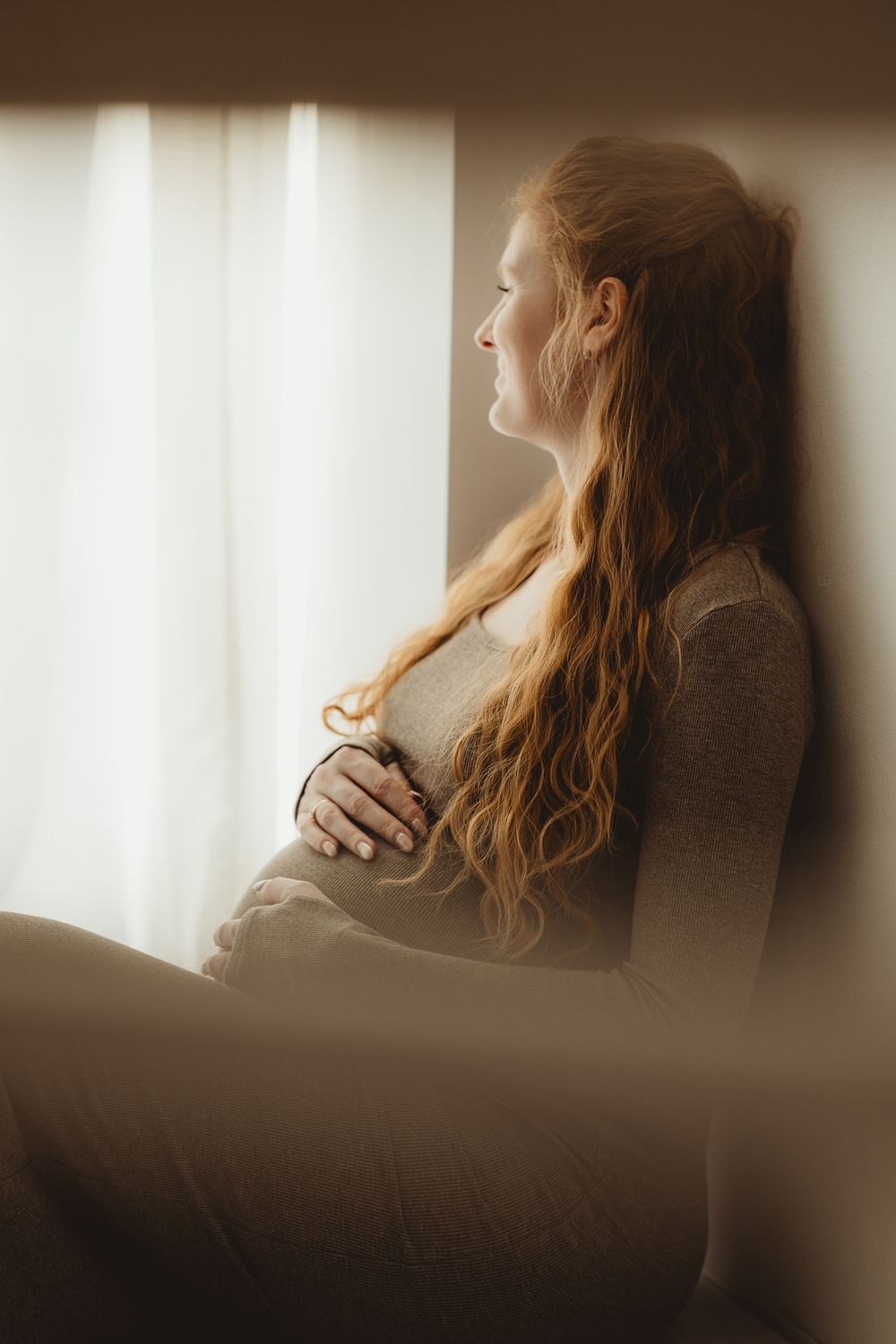 Artistic triptych photo series showing person with long red hair gazing thoughtfully by sunlit window in sepia tones.