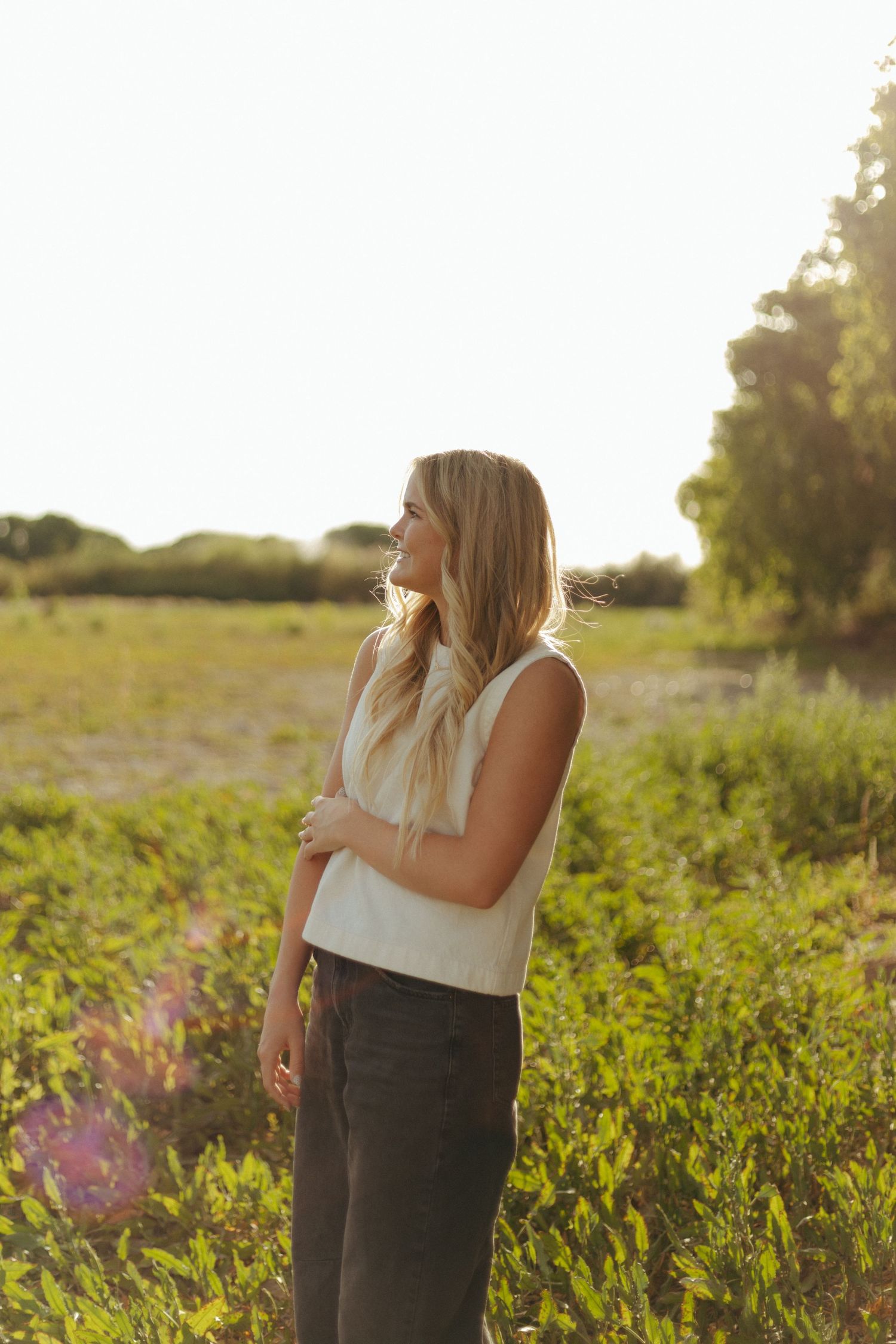 A person in casual attire stands in a sunlit meadow during golden hour.