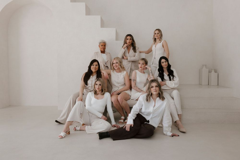 A group poses together wearing coordinated white outfits in a bright minimalist space with stairs.