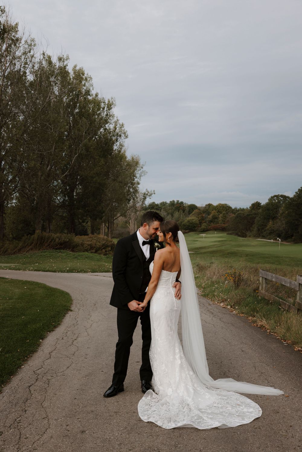 A wedding couple shares an intimate moment on a winding path surrounded by autumn trees.