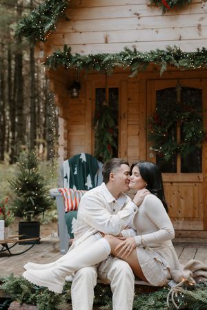 A romantic winter scene of a couple in white outfits sharing intimate moments on a wooden cabin porch.