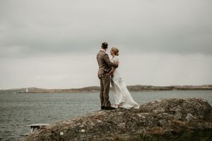 Romantic couple stands on rugged coastal cliffs overlooking a misty ocean landscape at sunset.