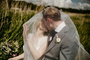 A romantic wedding couple embraces in a scenic outdoor setting with tall grass and natural light.