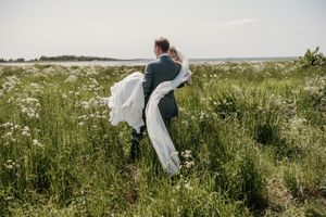 People in white clothing gather herbs and flowers in a lush green meadow on a sunny summer day.