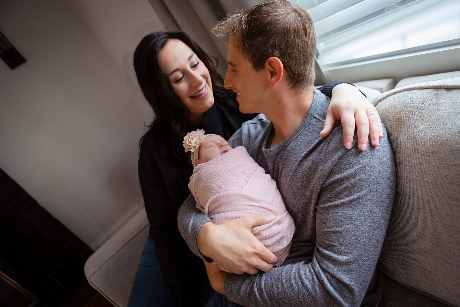 A husband and wife cuddle their newborn baby at their home during their comfortable photosession